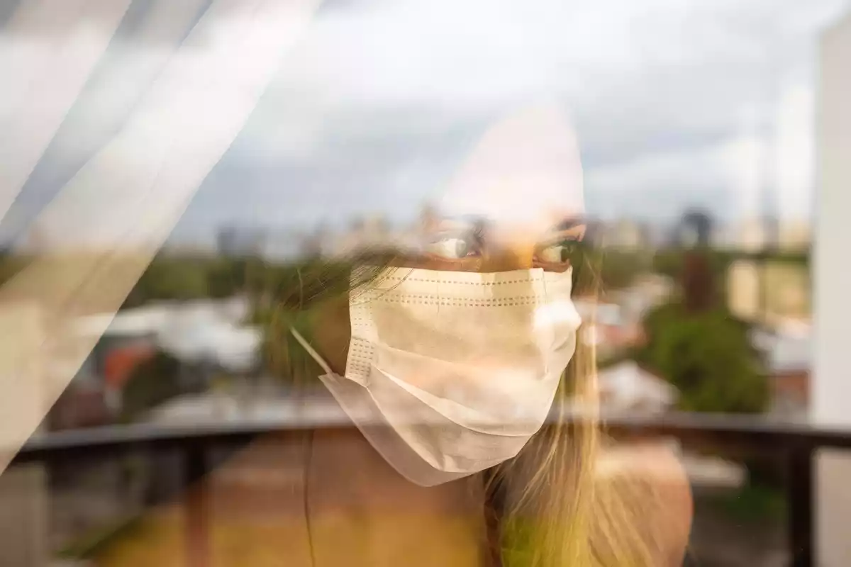 A woman wearing a mask looking outside a window