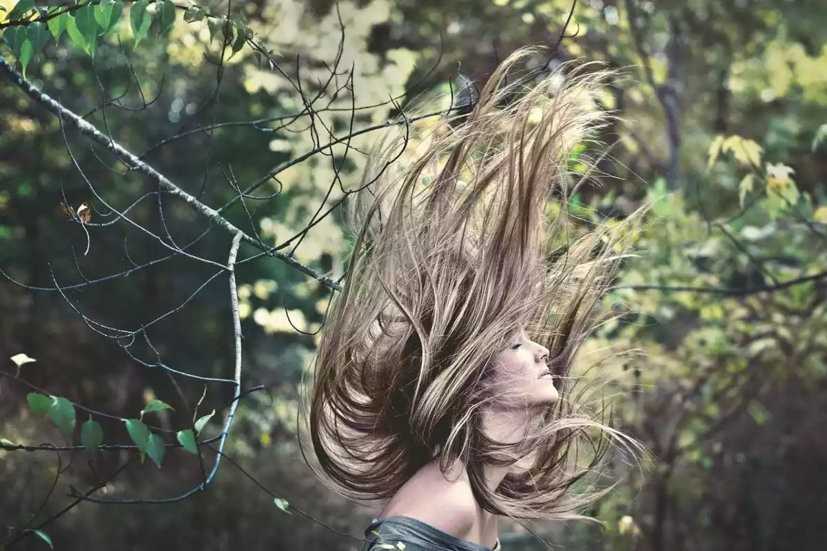 A woman shaking up his hair with a lot of trees in the background