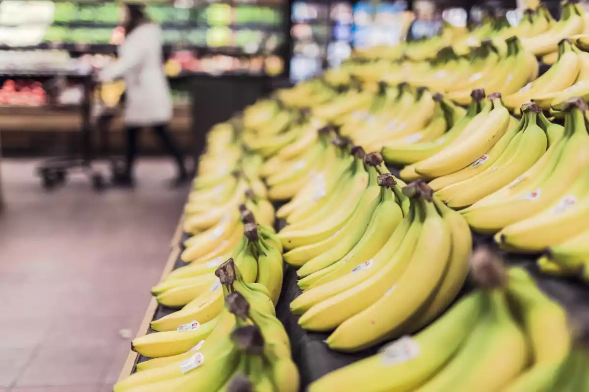Un puesto de bananas en un supermercado con una cliente detrás, comprando